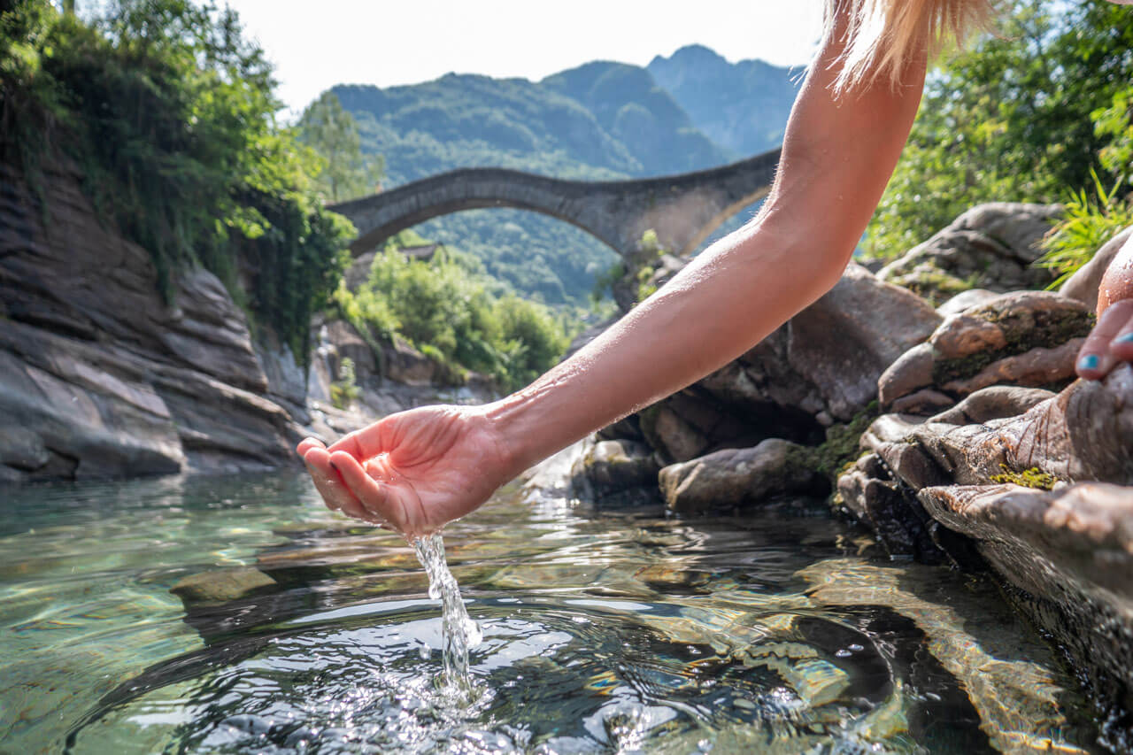 Hand schöpft klares Flusswasser im Verzascatal, Vokabeln üben in der Natur nach dem Unterricht