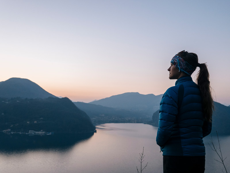 Frau mit Blick über den Luganersee bei Sonnenuntergang – stimmungsvolle Kulisse für eine Italienisch-Sprachreise nach Lugano in der Schweiz.