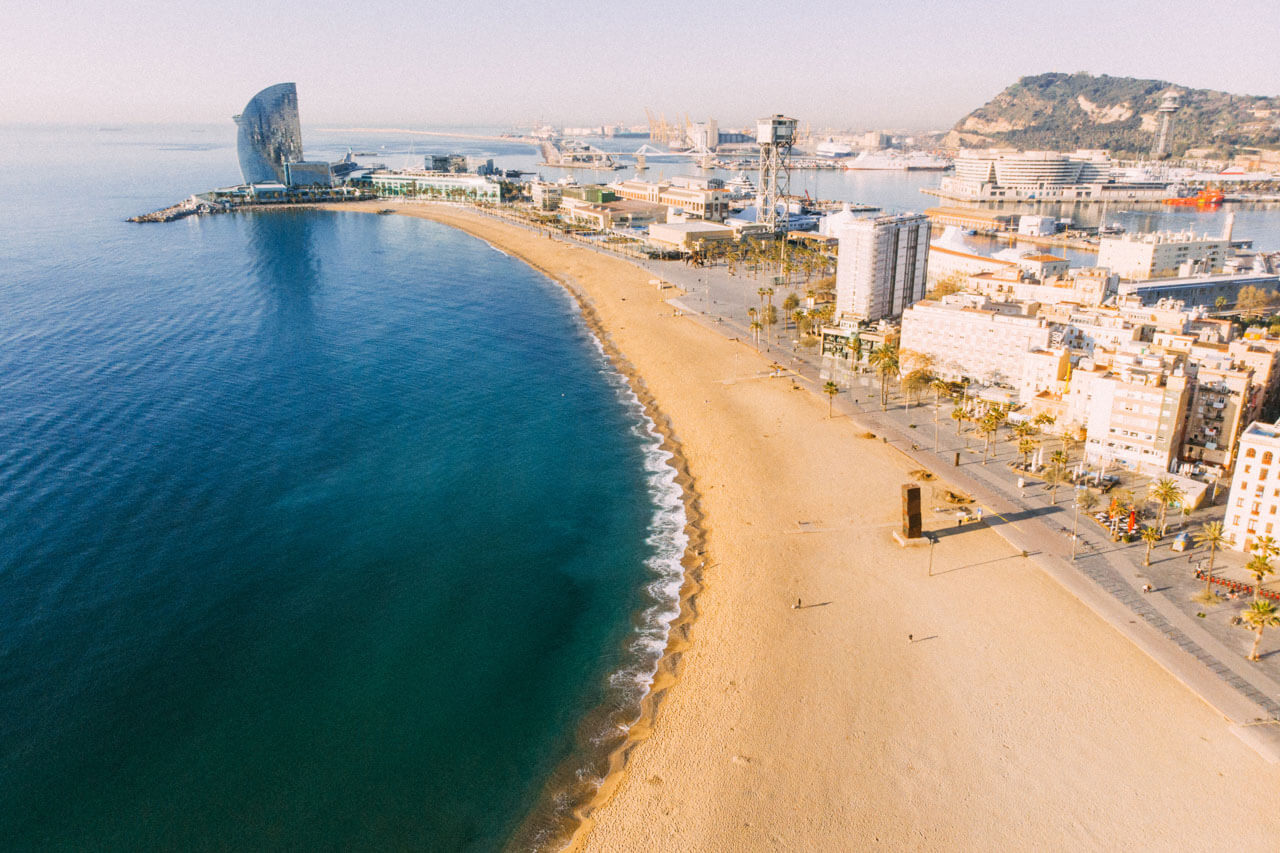 Breiter Stadtstrand La Barceloneta mit ruhigem Meer und Promenade, morgendliches Licht.