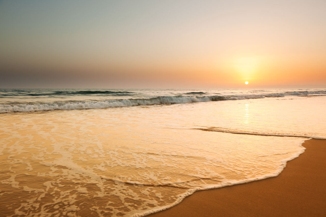 Sonnenuntergang am Strand von Cádiz: sanfte Wellen auf goldenem Sand, ruhige Atmosphäre an der andalusischen Küste.