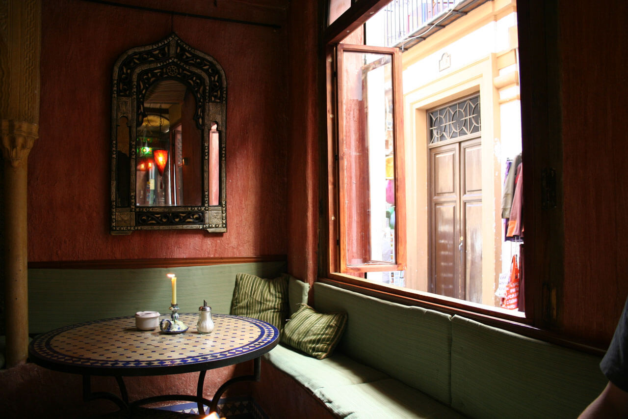 Orientalisch anmutendes Café in Granada mit Mosaiktisch, Polsterbank und offenem Fenster zur Gasse.