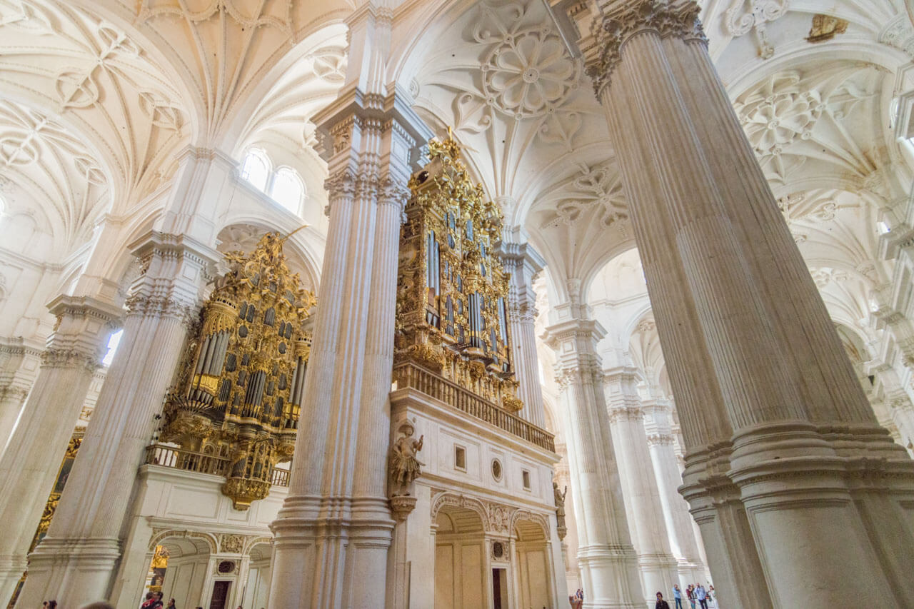 Innenraum der Kathedrale von Granada mit hohen weißen Säulen und vergoldeten Orgeln.