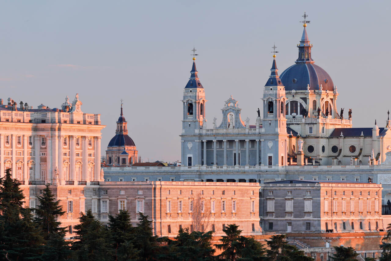 Blick auf die Almudena-Kathedrale neben dem Königspalast von Madrid im warmen Abendlicht.