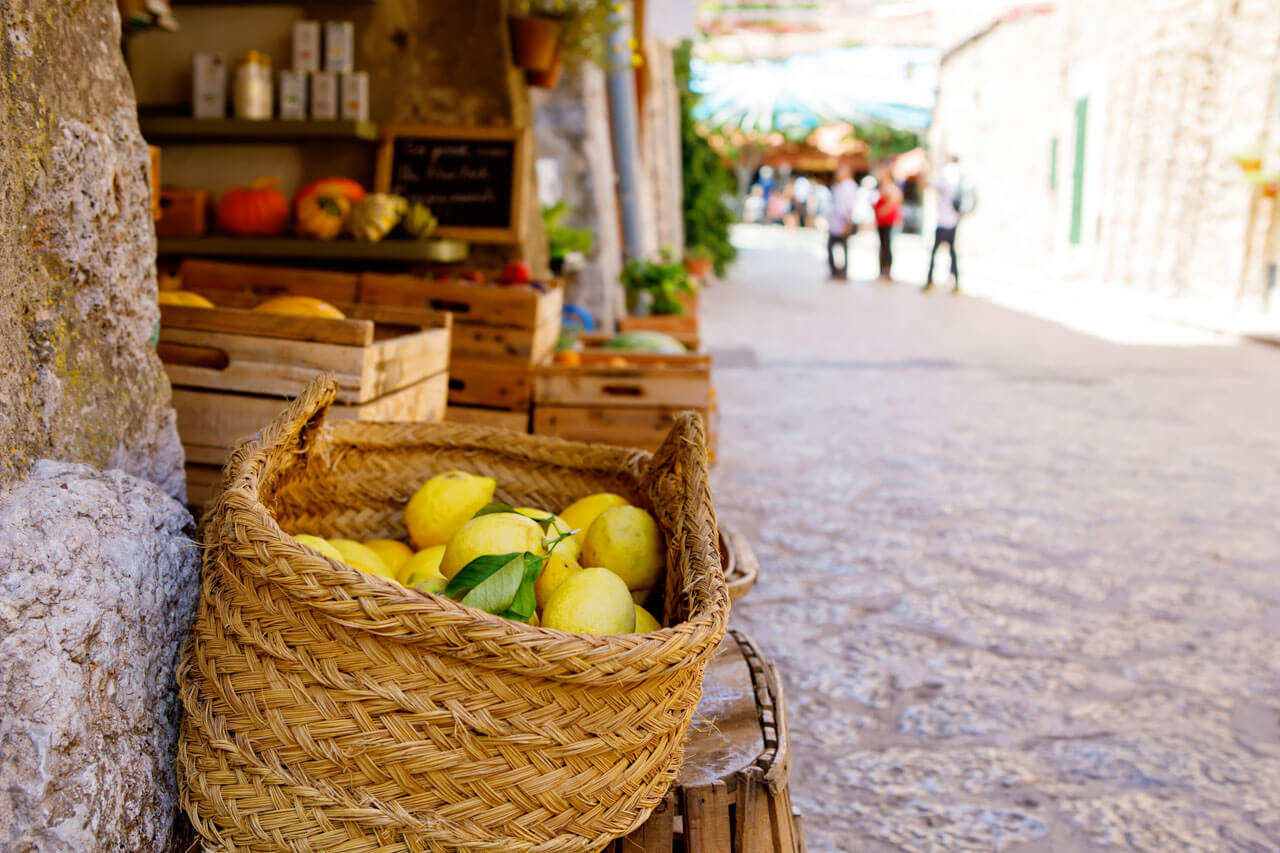 Geflochtener Korb voller Zitronen vor einem Marktstand in mallorquinischem Dorf.
