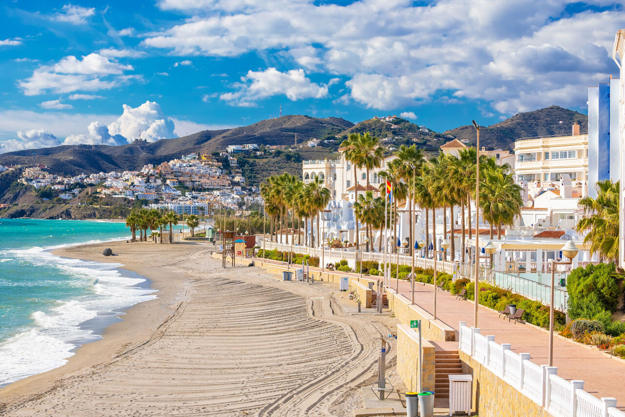 Promenade von Nerja mit Palmen, breitem Sandstrand und Blick auf die Hügel Andalusiens