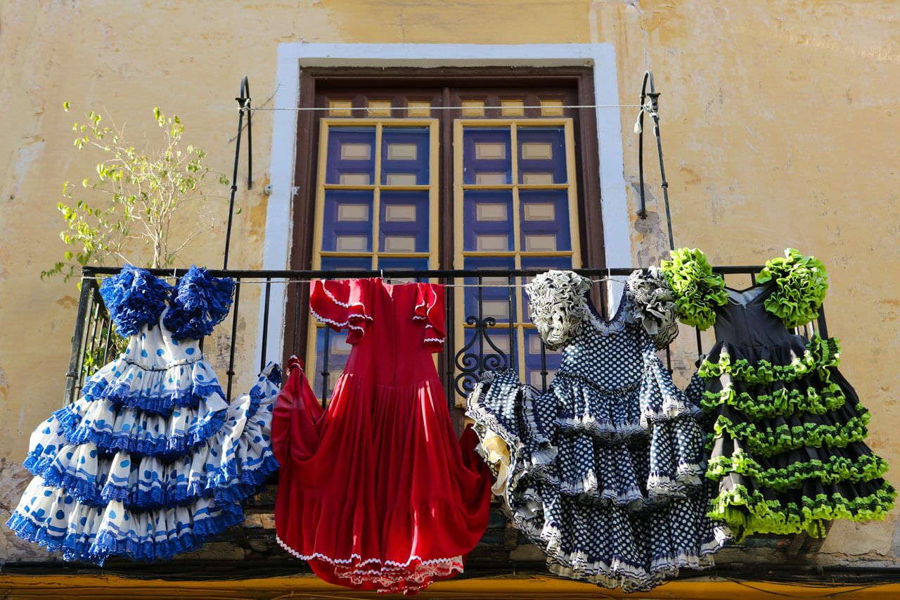 Bunte Flamenco-Kleider in Rot, Blau und Schwarz hängen an einem Altstadtbalkon.