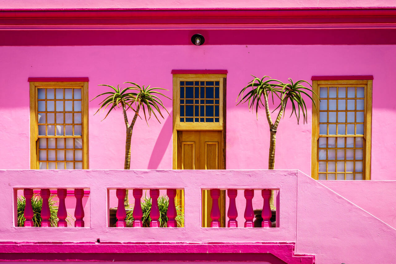 Pinkfarbene Fassade mit Palmen und Holztür, Grammatik im Kontext beschreiben.