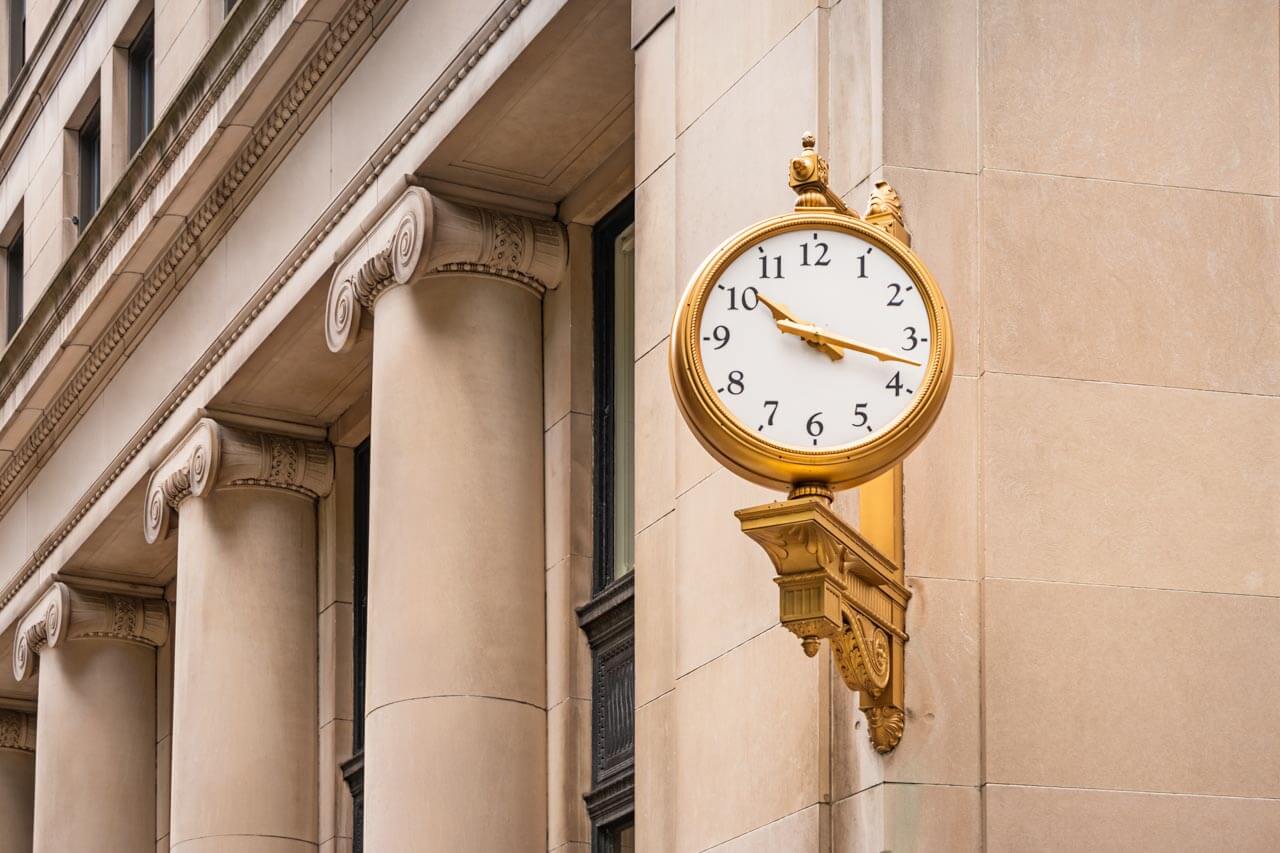 Historische goldene Uhr an Steinfassade, Grammatik trainieren mit Zeitangaben.