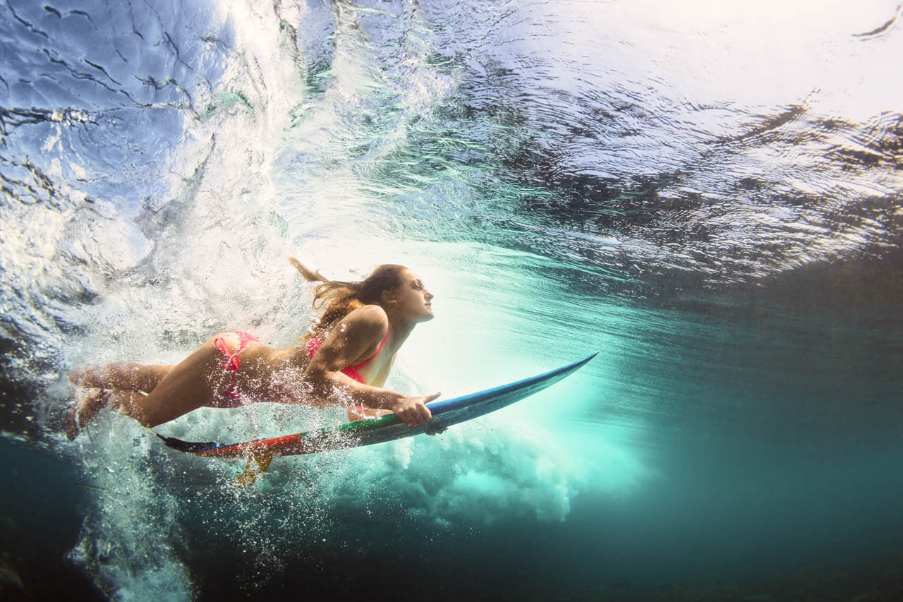 Surfende Person taucht unter der Welle. Sprachkurs am Meer.