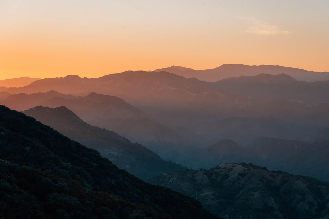 Abgestufte Bergsilhouetten im warmen Abendlicht mit Nebelschleiern.