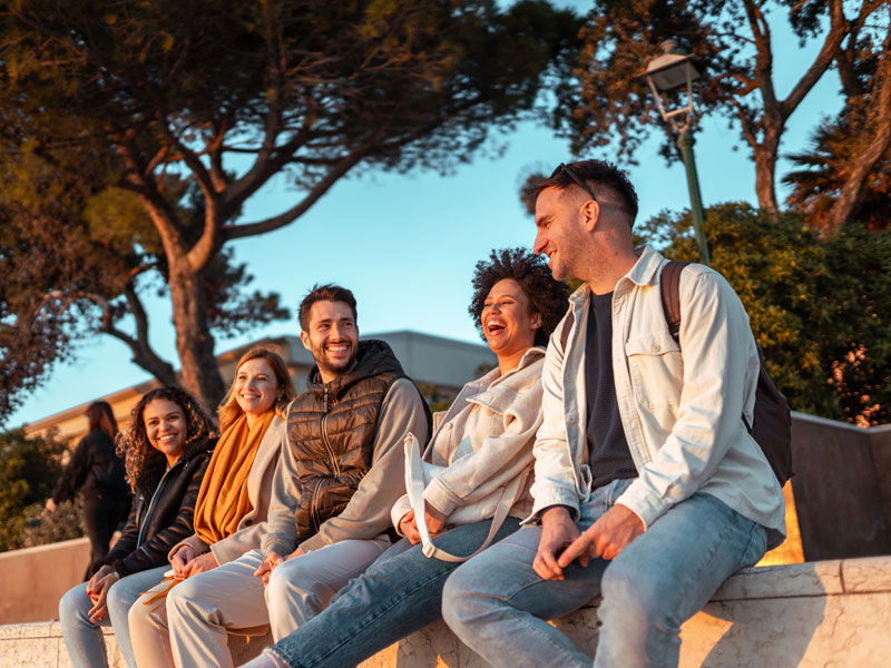 Gruppe Erwachsener lacht gemeinsam im Sonnenuntergang während einer Sprachreise.
