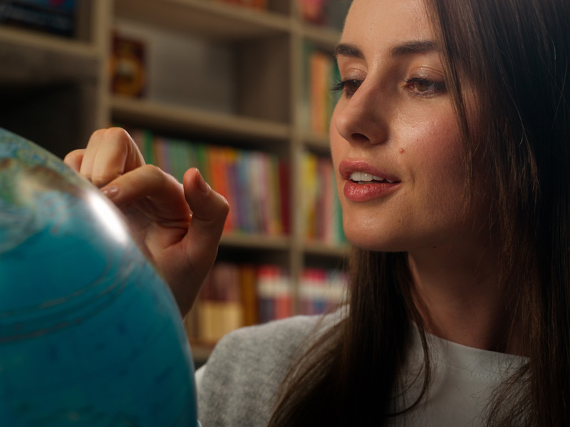 Frau betrachtet interessiert einen Globus und plant ihre Sprachreise ins Ausland.