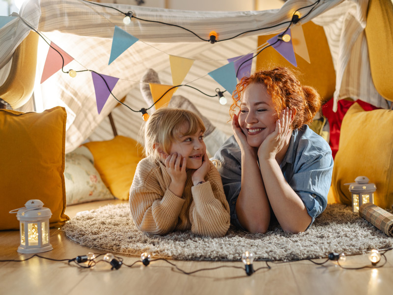 Junge Frau und Kind lachen gemeinsam in gemütlicher Umgebung bei einer Gastfamilie.