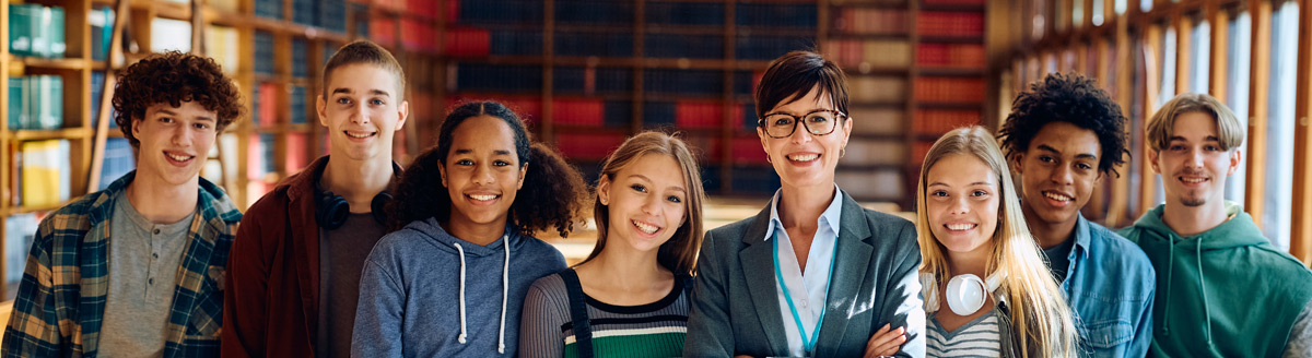 Schulklasse mit Lehrerin lächelt gemeinsam in einer Bibliothek im Ausland.
