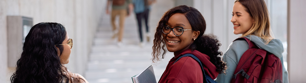 Drei Jugendliche mit Rucksäcken lächeln auf dem Weg zur Sprachschule.