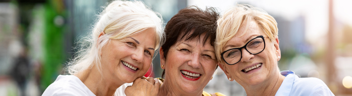 Drei Seniorinnen lächeln fröhlich bei einer Sprachreise im Ausland.